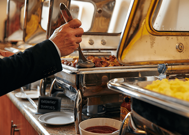 Person scooping potatoes from a buffet of catering for a corporate event